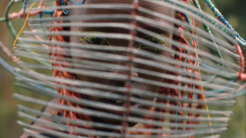Image from Neptune Frost - A close up of a woman looking at the camera from behind a wicker headdress